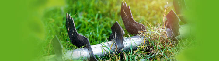 Nahaufnahme eines Vertikutierers mit geschärften Klingen auf grünem Gras.